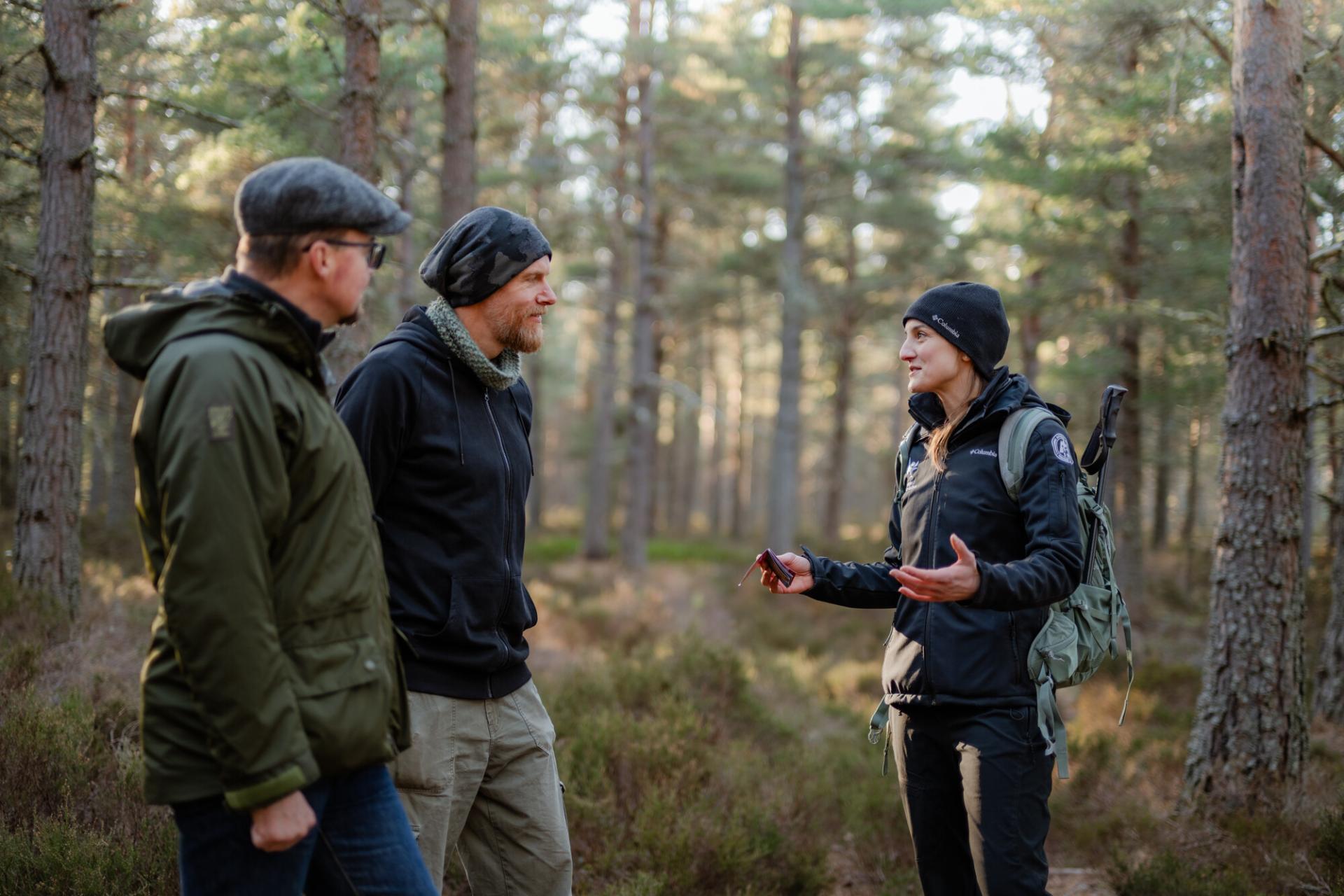 A Park Authority ranger engages with two visitors to the National Park about the dangers of wildfire risk in the woods. They are holding a small fire prevention leaflet and wearing a National Park uniform.