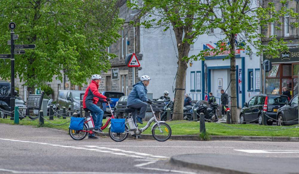 A couple ride ebikes on the streets of Grantown on Spey.