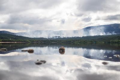 Smoke coming from the woods behind a calm Loch Morlich.