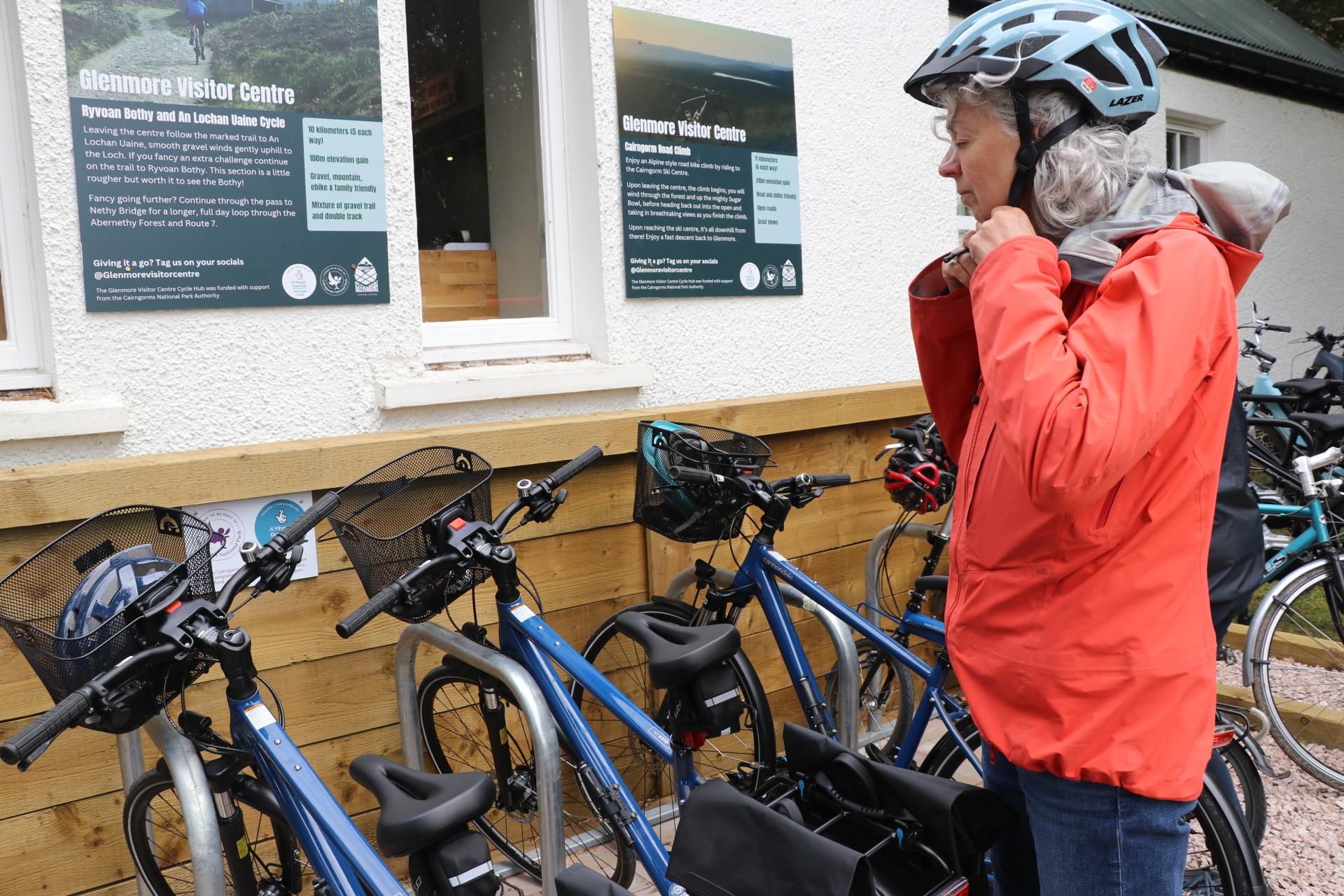 A person puts on a bike helmet while looking at bikes locked up outside a building