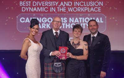 Four people standing on a stage, with two in the centre holding an award.