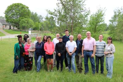 Group of people standing in grass smiling, with trees in background.