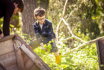 A child with glasses, wearing yellow wellies, foraging in the woods.