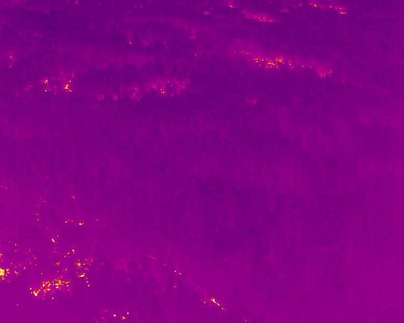 Thermal drone image showing hot spots from wildfire in foreground and background.