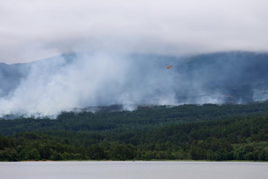 Orange helicopter flies over the trees and smoke near Loch Morlich at the site of the Glenmore wildfire