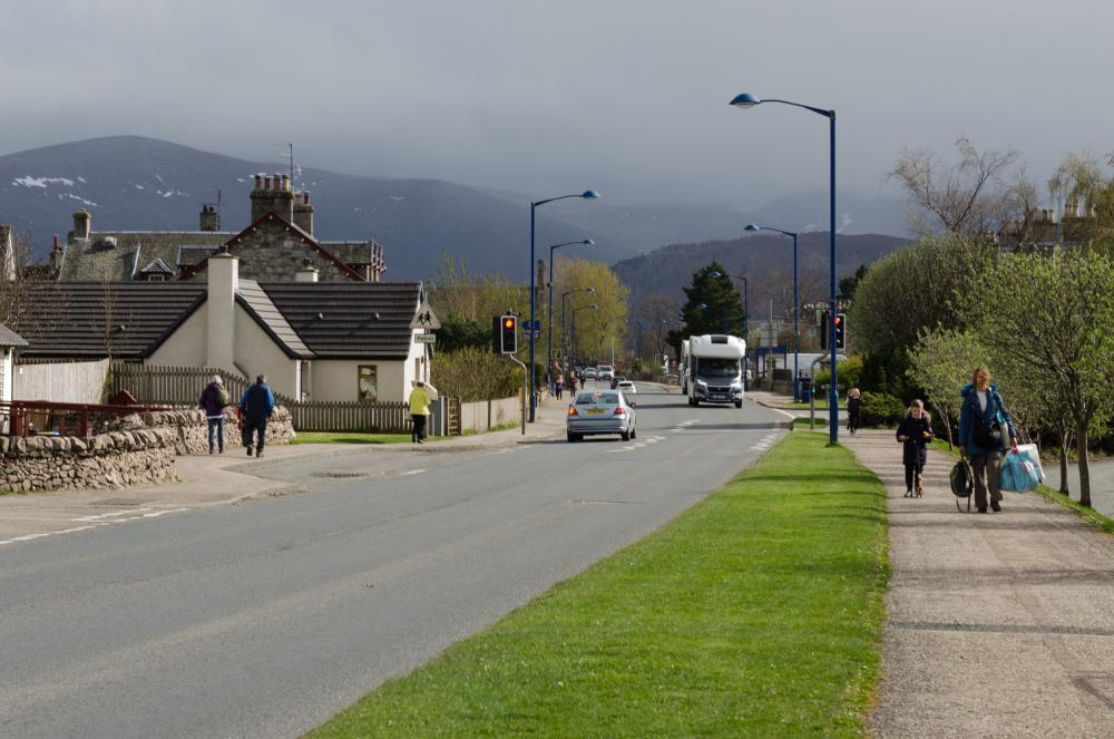 Looking along Grampian road in Aviemore with pedestrians walking on the pavement on either side