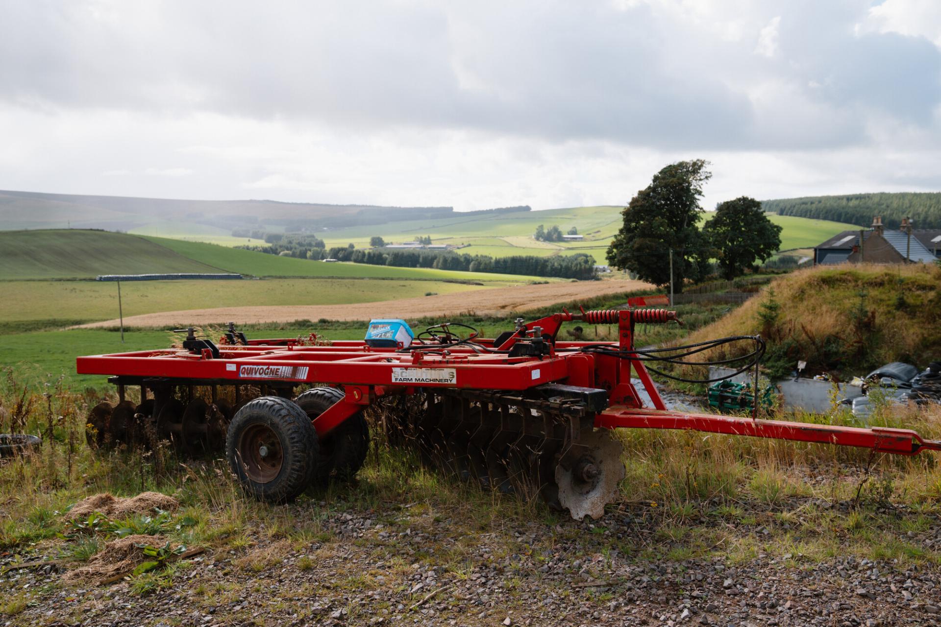 Agricultural machinery with a backdrop of fields and hills.