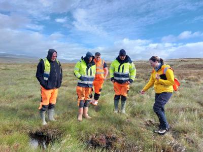 A woman in a yellow jacket shows four men wearing hi-vis jackets and wellies key habitats and species on a peat bog in the Cairngorms
