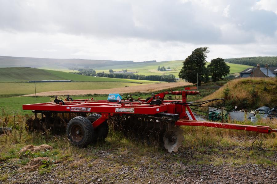 Agricultural machinery with a backdrop of fields and hills.