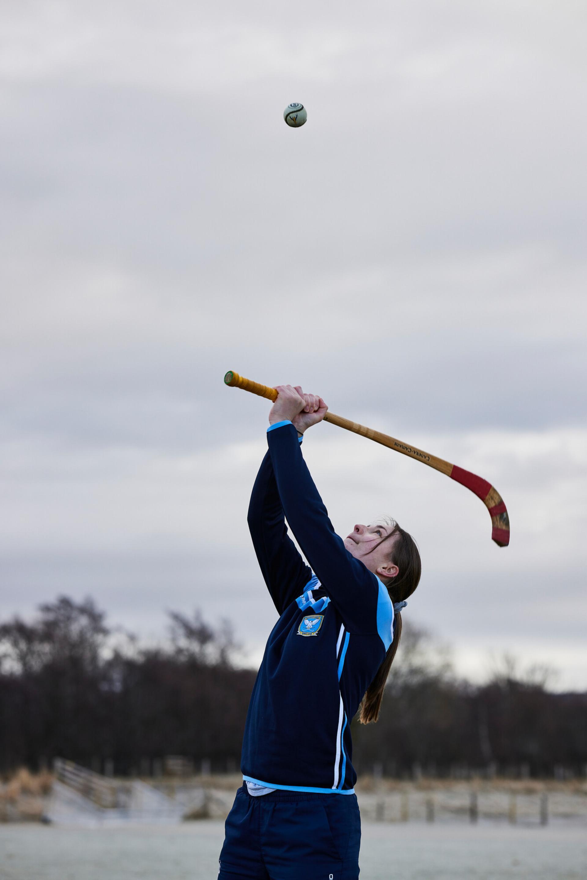 Shinty player swinging their stick or caman at the ball above their head