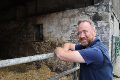 Man leaning on a gate to a cow shed, looking at the camera and smiling