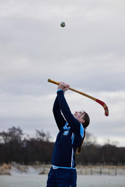Shinty player swinging their stick or caman at the ball above their head