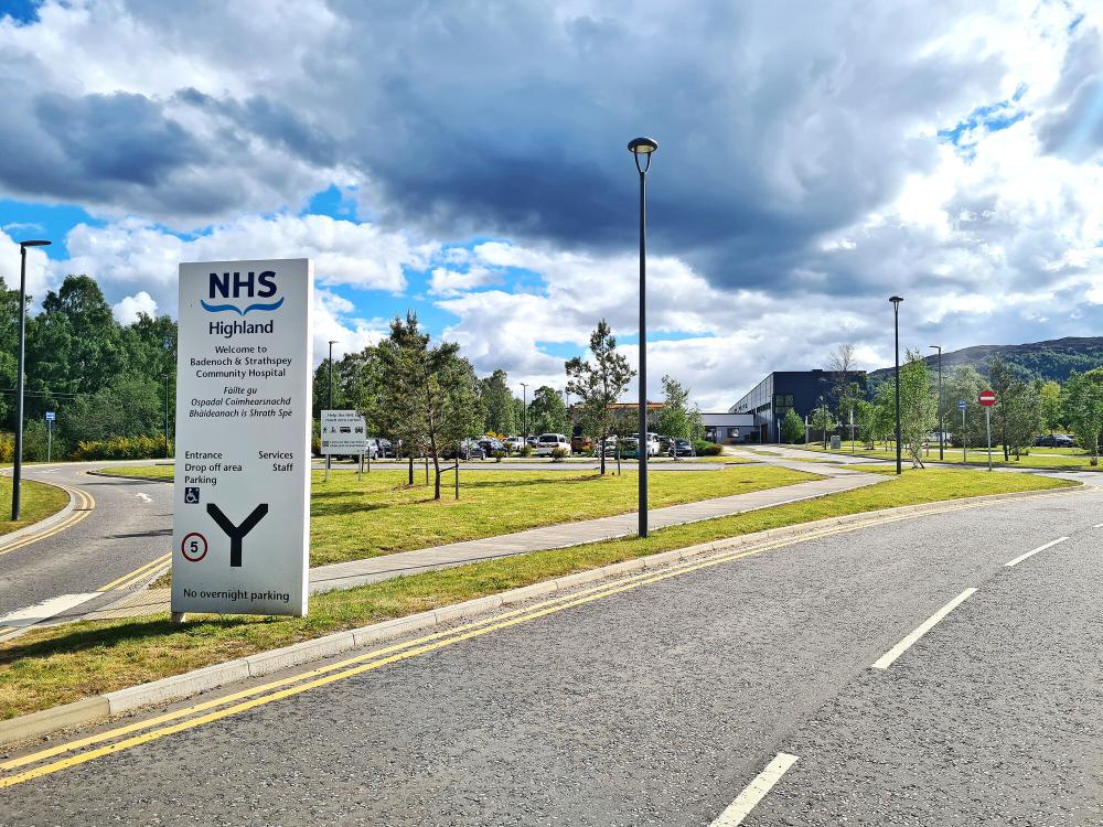 The road leading to Badenoch and Strathspey Community Hospital with NHS welcome sign with directions.