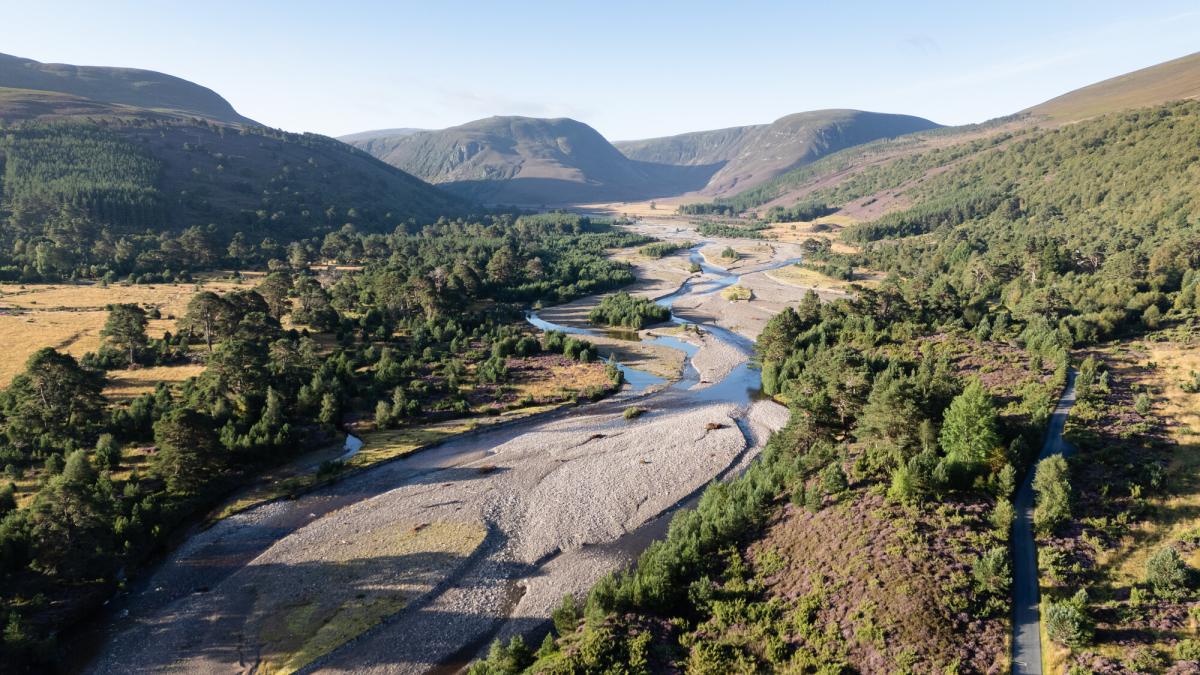 An aerial view of the river Feshie running through Glenfeshie with trees on both sides and surrounding mountains
