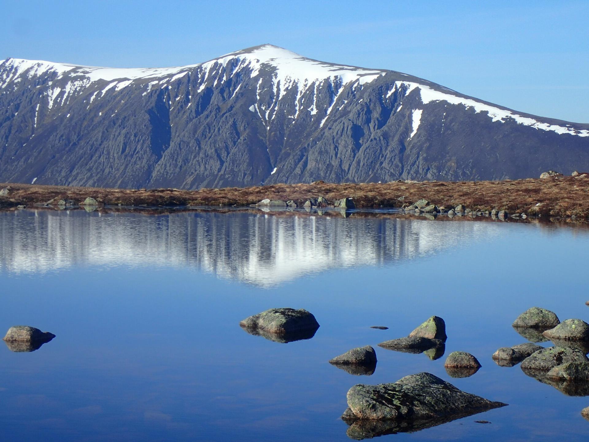 Calm lochan in the mountains with reflection of distant mountain.