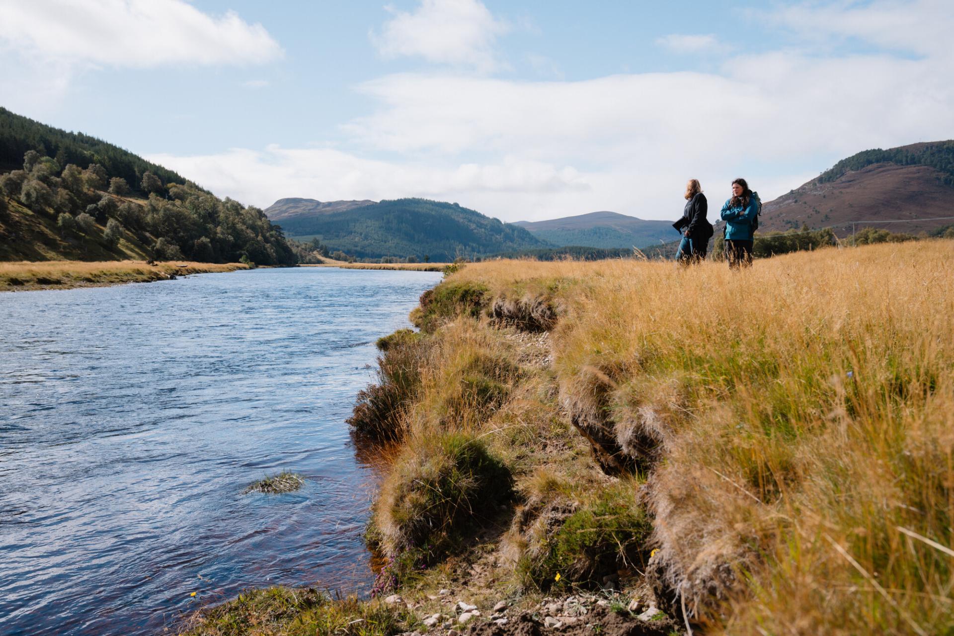 Two people standing on the banks of the River Dee.