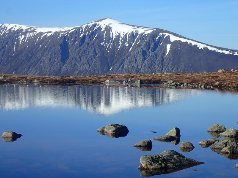 Calm lochan in the mountains with reflection of distant mountain.