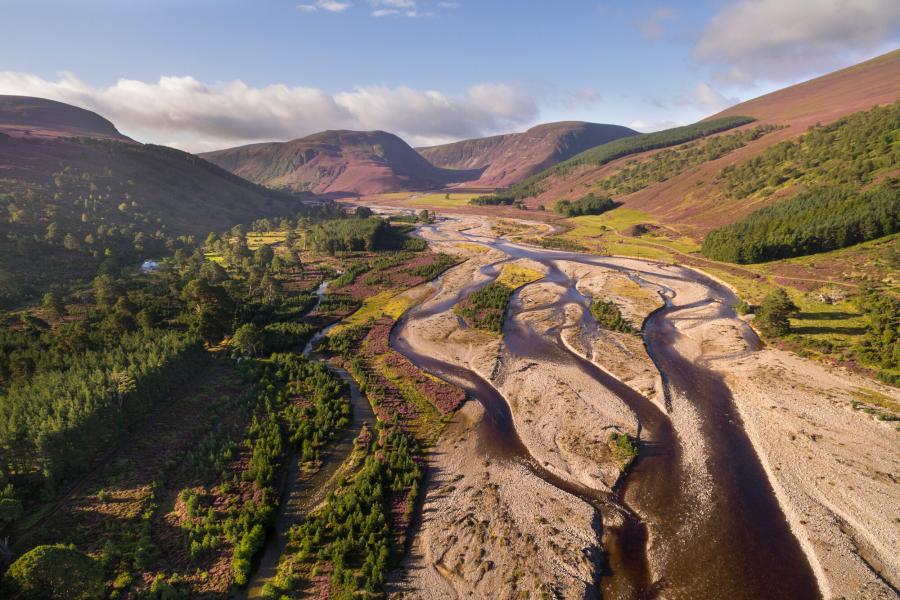 Aerial view of Glensfeshie showing the river Feshie with trees on either side and surrounding mountains.