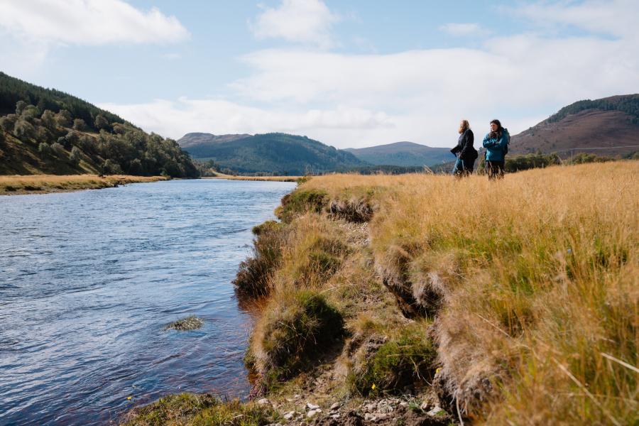 Two people standing on the banks of the River Dee.