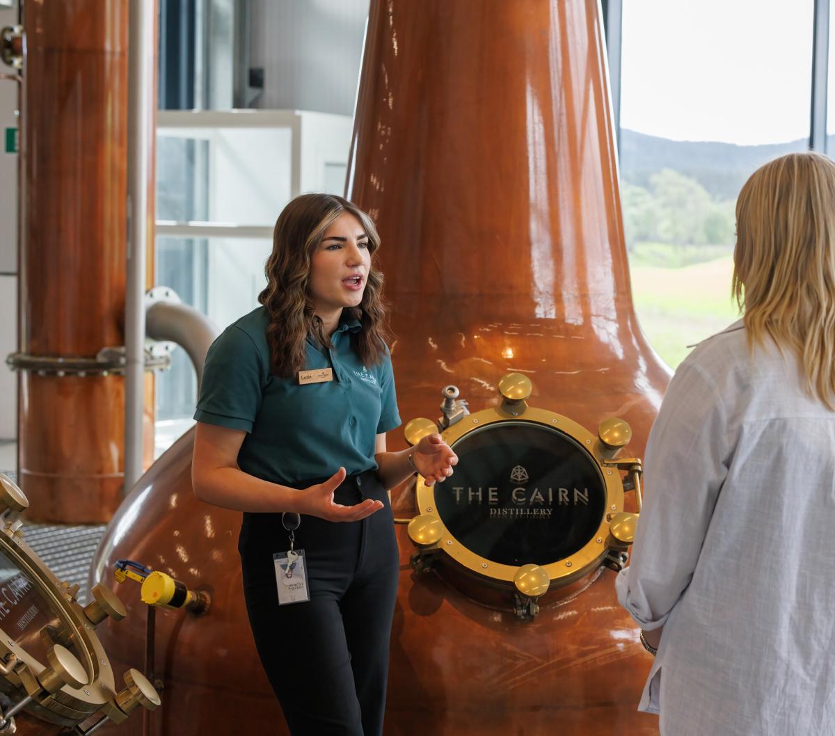 People on a tour of The Cairn Distillery with whisky stills in the background