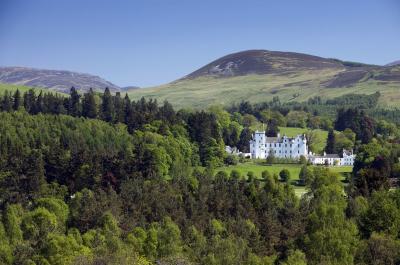 All white Blair castle surrounded by forest with mountains in the background.