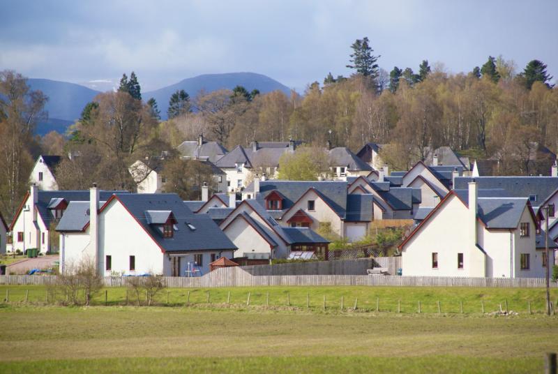 Looking over a field to houses with woodland and mountains in the background.