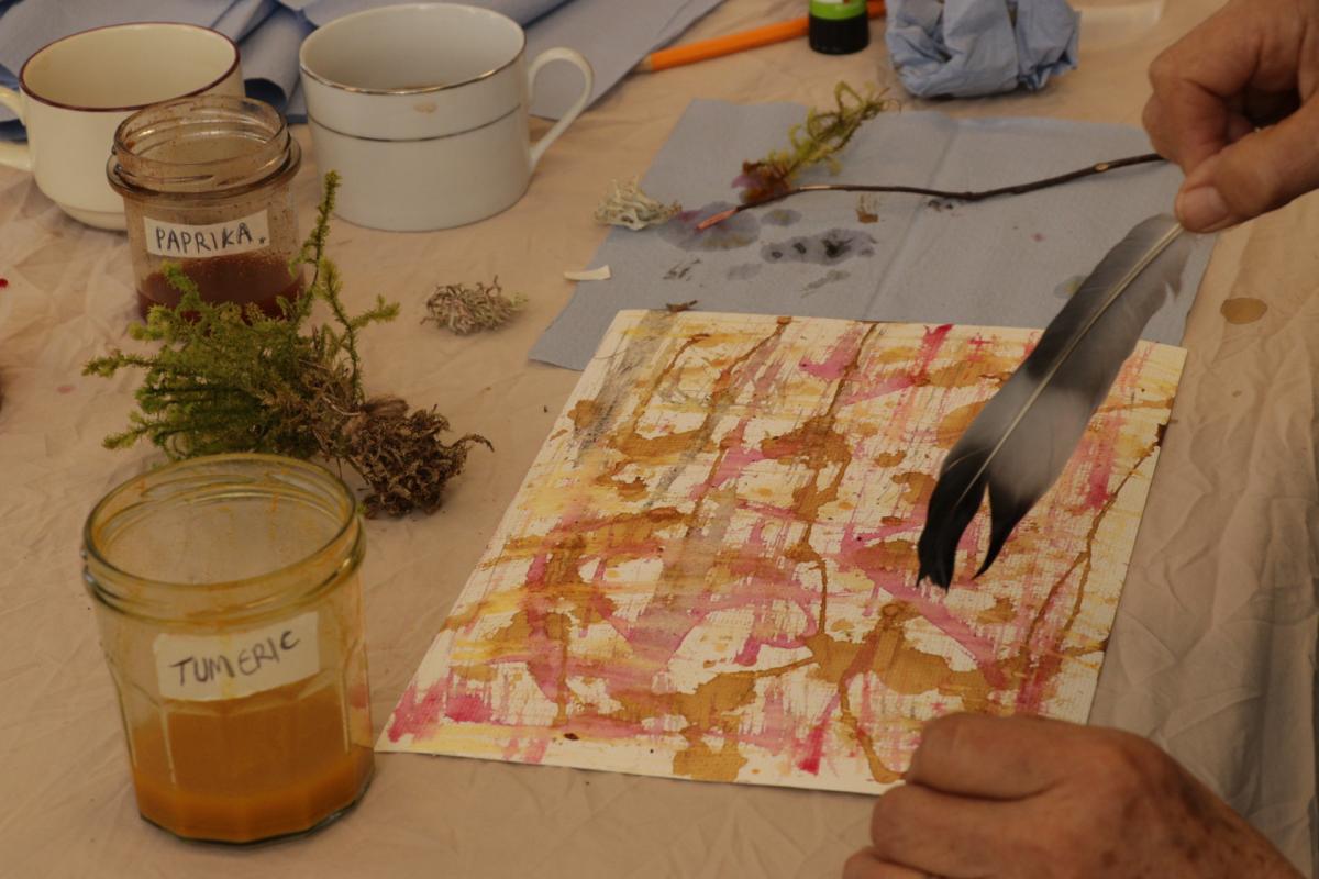 A hand holding a feather making watercolour art