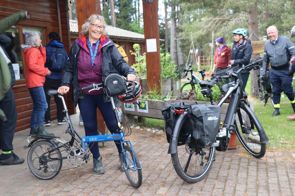 A person smiles next to a folding and electric bike