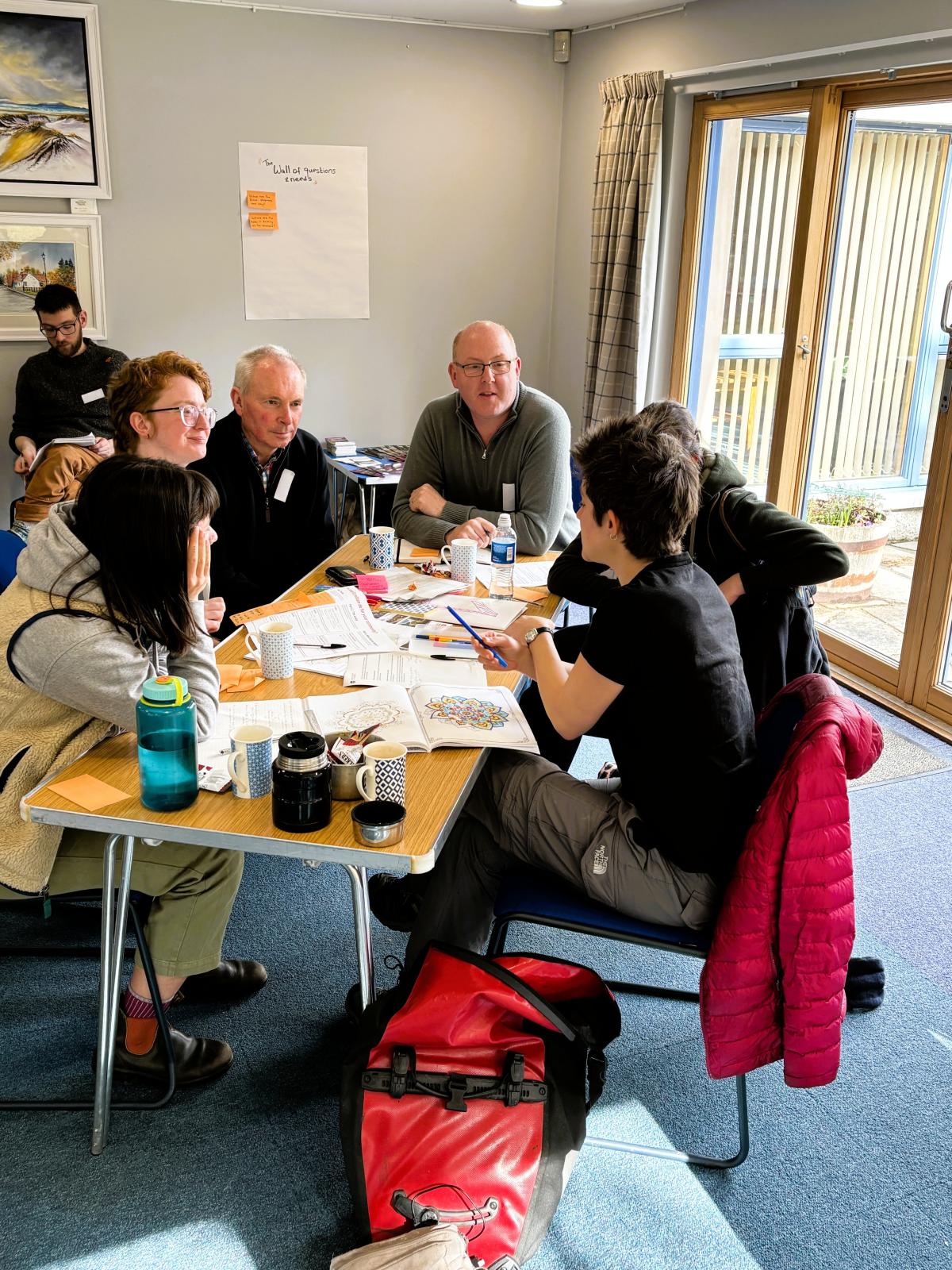 Five members of the Communities Fund panel plus a facilitator from Involve discuss options around a wooden tressle table in Boat Hall