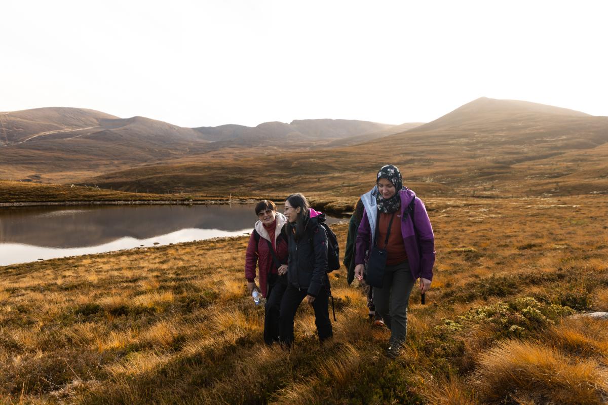 Three people from the Community Champion Scheme walking through heather with a lochan in the background.