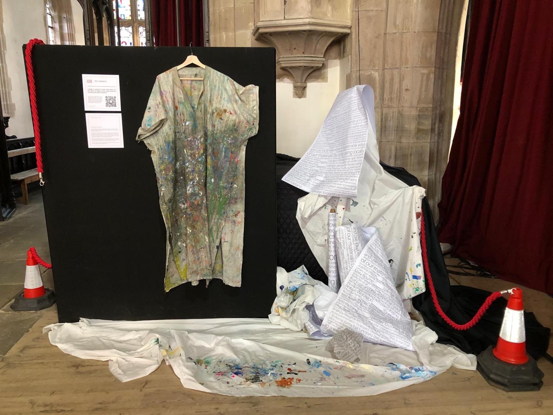 Several garments splattered with paint hang in a church hall