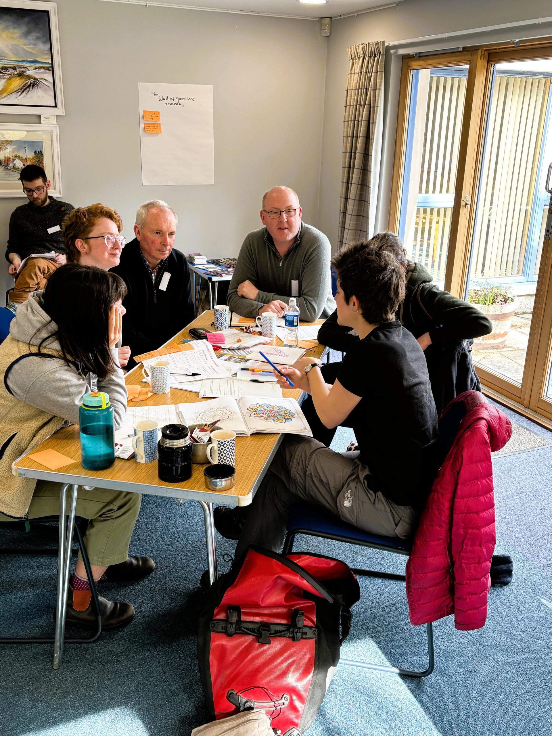 Five members of the Communities Fund panel plus a facilitator from Involve discuss options around a wooden tressle table in Boat Hall