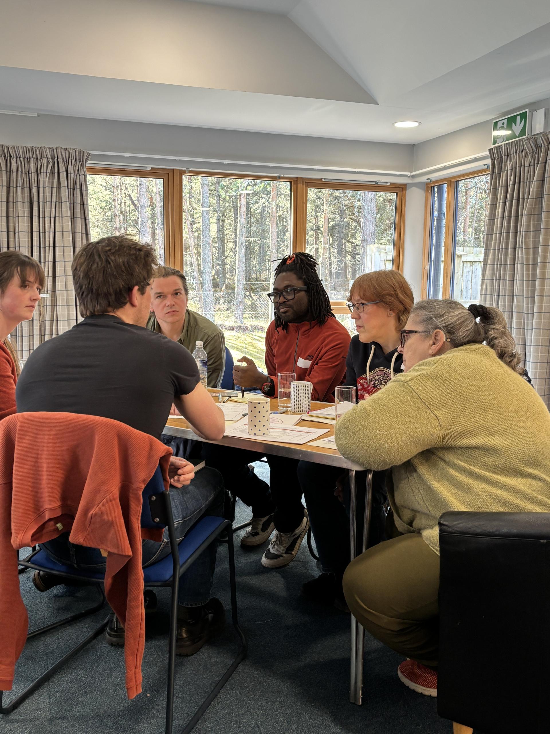 Five members of the Communities Fund panel plus a facilitator from Involve discuss options around a wooden tressle table in Boat Hall