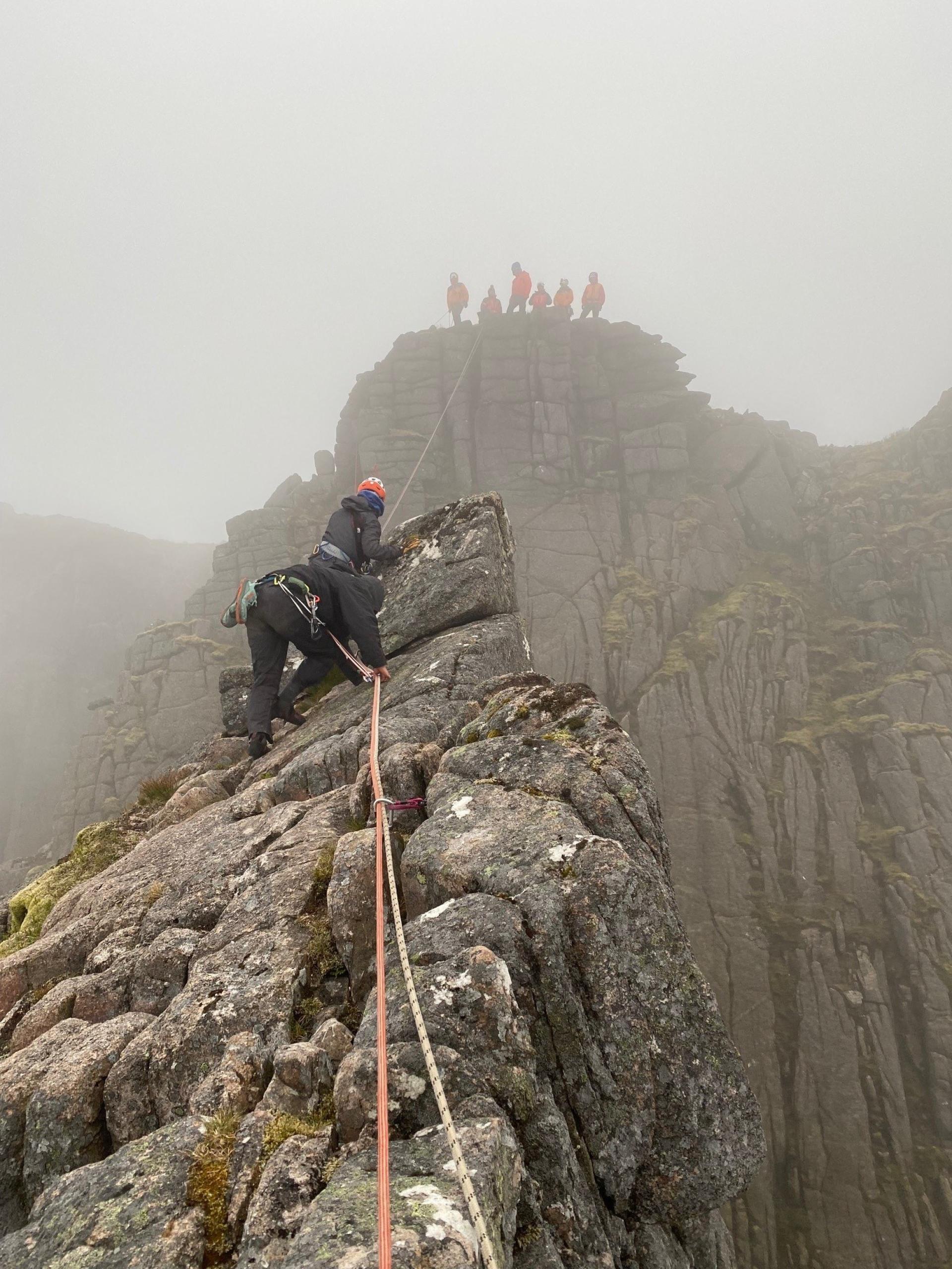 Two groups of mountain rescue volunteers with rope between two cliff tops.