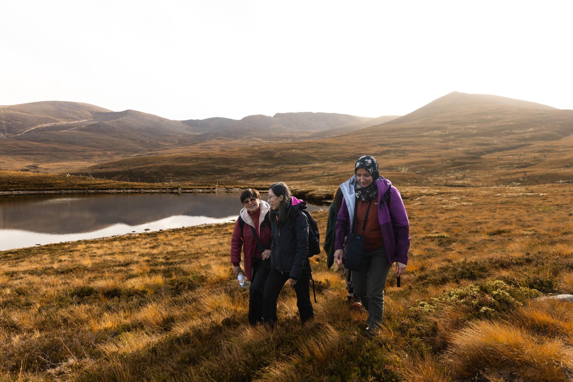 Three people from the Community Champion Scheme walking through heather with a lochan in the background.