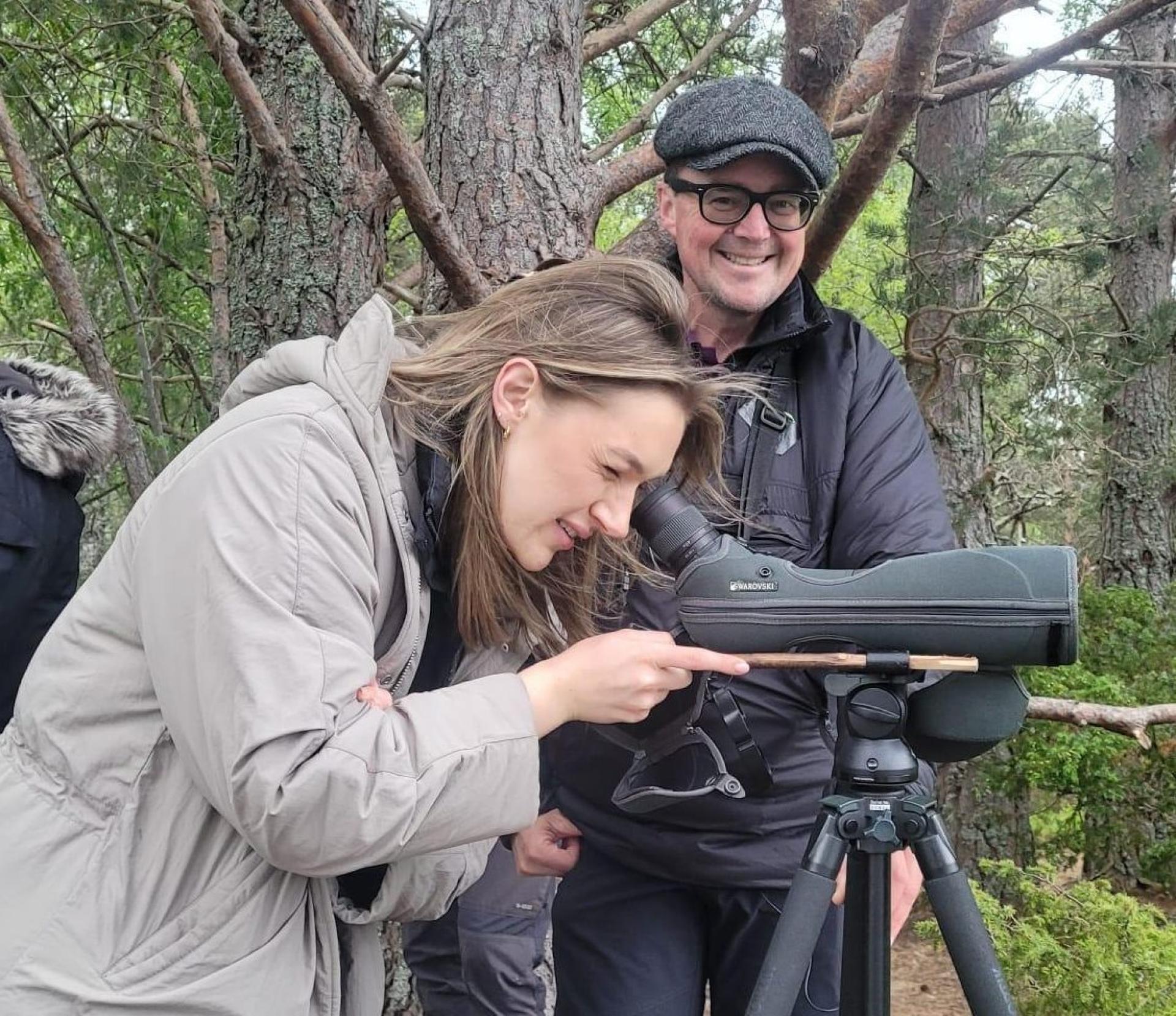 A person looking through a lense in a ling grey coat