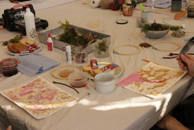 People taking part in crafts with two sheets of paper and crafting materials sourced from nature, branches and glue sticks.