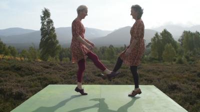 Two females doing a traditional dance with mountain landscape in background.