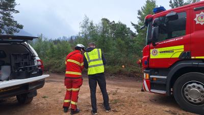 two people stand beside fire engine and pickup truck, with smoke in background.