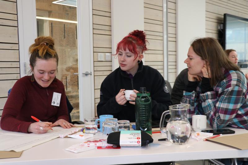Three people sit at a table with paper and pens
