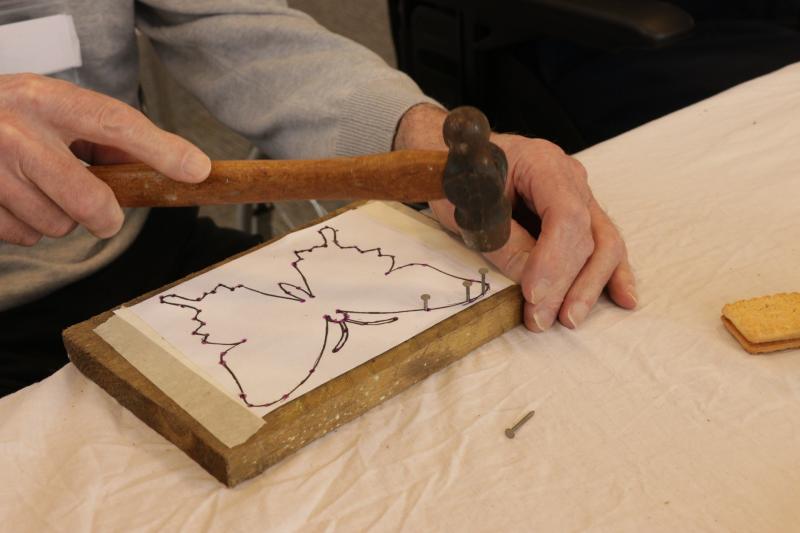 A pair of hands holding a hammer over an artwork in progress of a butterfly