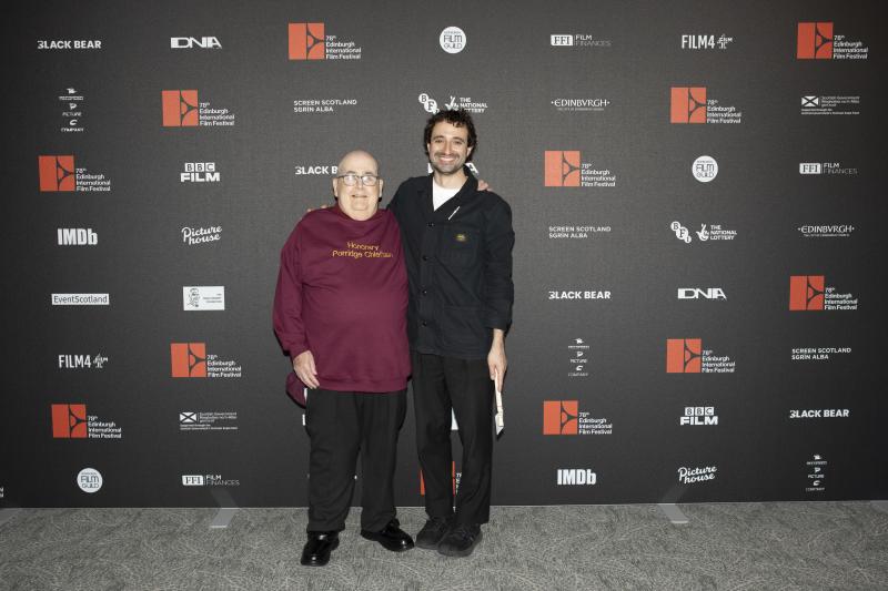 Two men standing in front of a banner of logos at the Edinburgh International Film Festival.