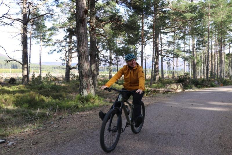 Image of Sarah Rathbone smiling as she rides along a trail through woodland in the Cairngorms National Park,