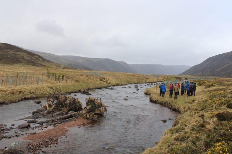 Image of members of the River Dee Trust stood on the river bank on a site walk and talk with mist covered mountains in the background.