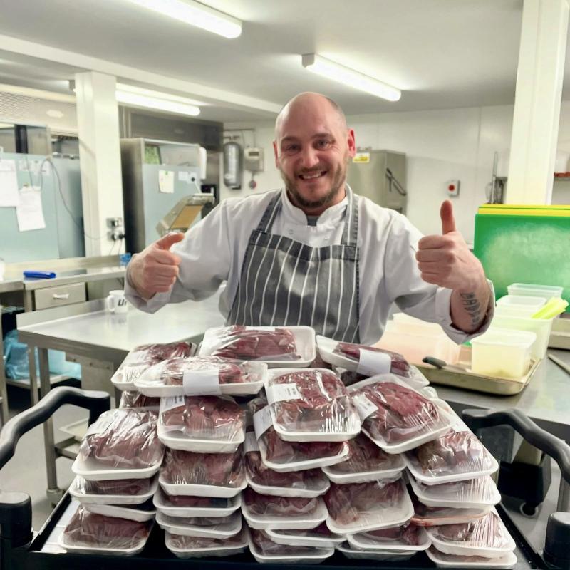 Chef with thumbs up behind a large pile of wrapped venison meat.