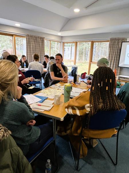 Four members of the Communities Fund panel plus a facilitator from Involve discuss options around a wooden tressle table in Boat Hall