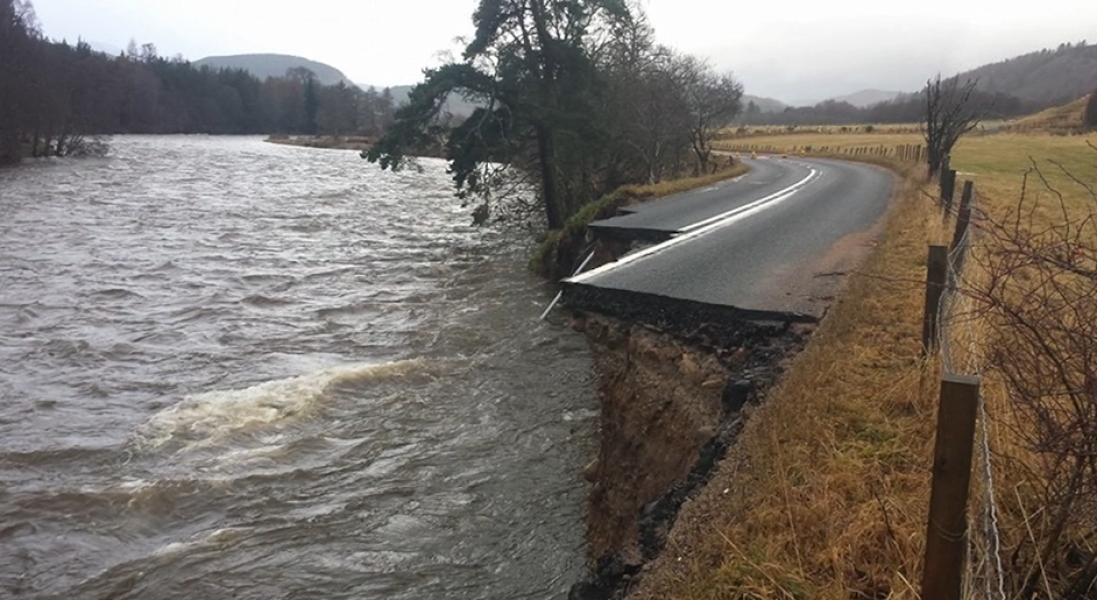Image of a road crumbling into a high river, with half of the left lane gone.
