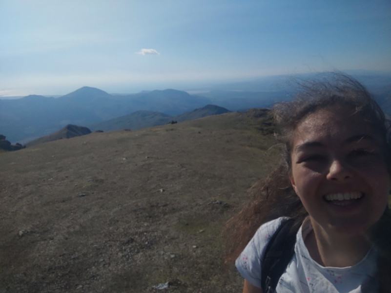 A person smiling at the top of a mountain