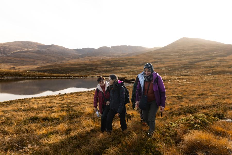 Three people from the Community Champion Scheme walking through heather with a lochan in the background.