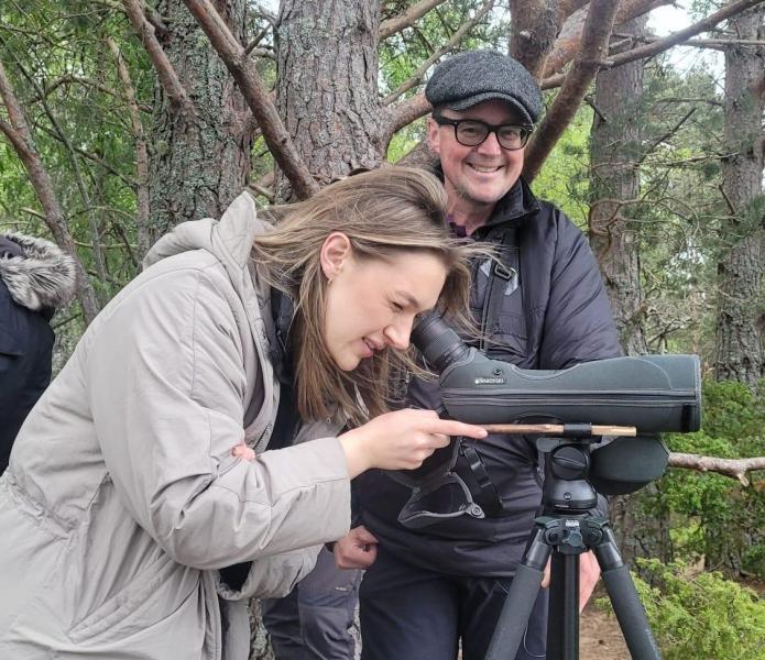 A person looking through a lense in a ling grey coat